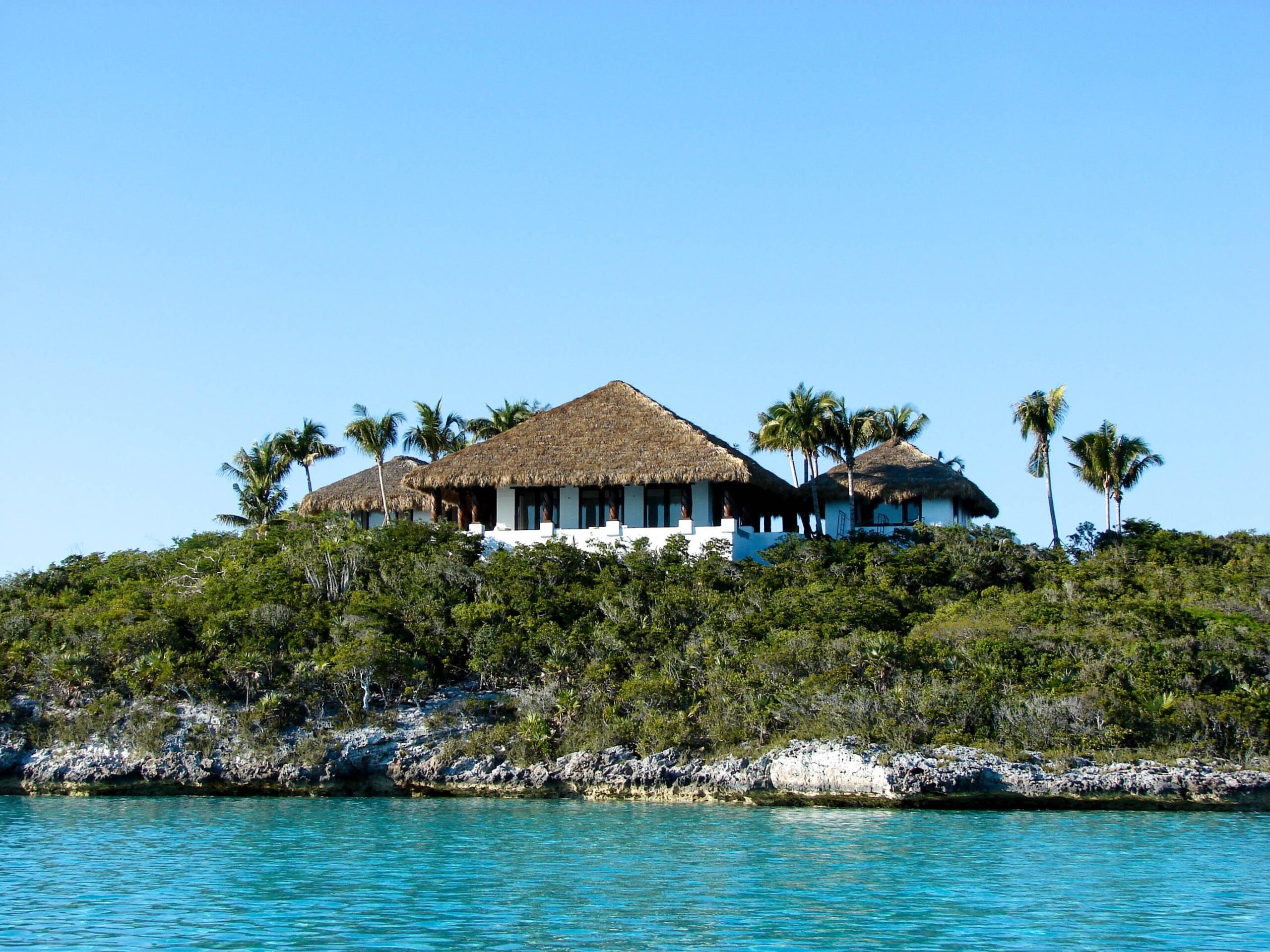 Tiki hut structures with thatched roofs on a lush island landscape, showcasing natural and synthetic thatch roofing options by The Tiki Hut Company.