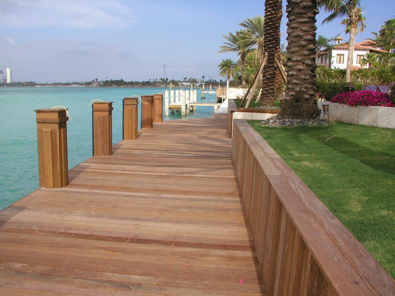 Wooden dock extending over turquoise water, surrounded by palm trees and lush greenery, showcasing a picturesque setting for tiki hut projects and outdoor leisure.