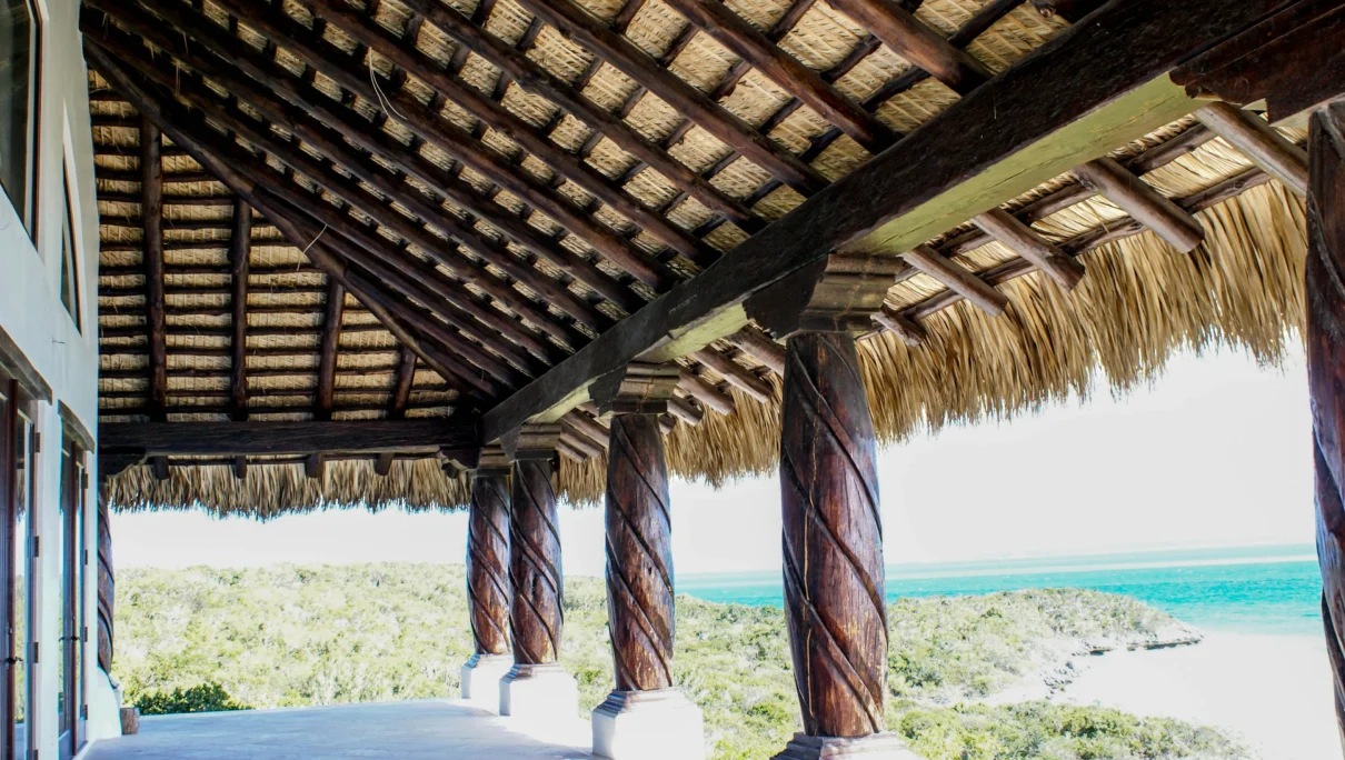 Thatch roof structure with wooden columns overlooking a coastal landscape, illustrating custom tiki hut solutions for beach properties.