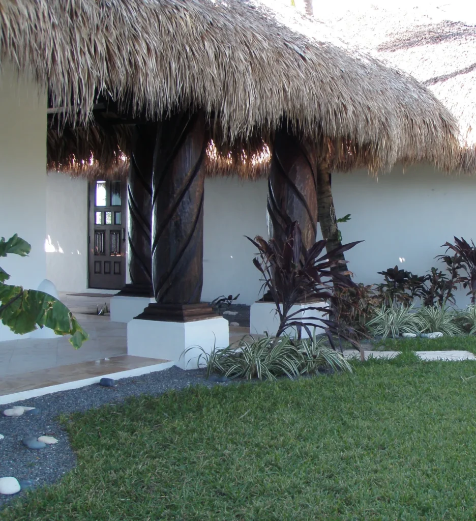 Custom tiki hut with thatched roofing, decorative wooden columns, and landscaped garden, enhancing beachfront property aesthetics.